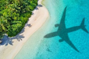Travel concept with airplane shadow and tropical beach. Tropical paradise and beach holiday conceptual image.