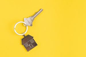 Home key with house keyring or keychain on solid yellow background using as home ownership, mortgage or buy and sell property and real estate.