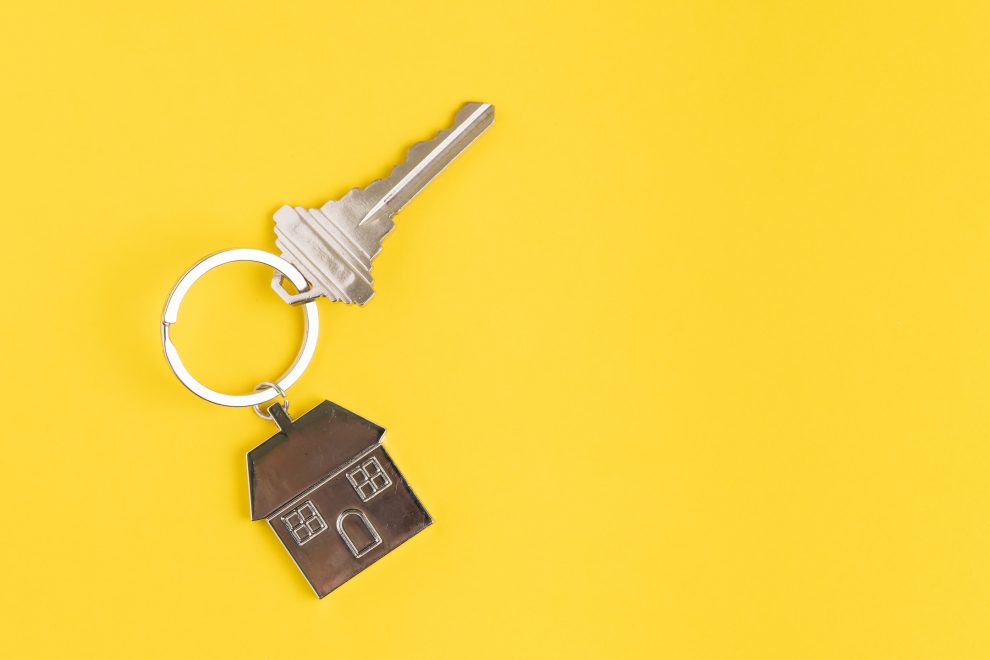 Home key with house keyring or keychain on solid yellow background using as home ownership, mortgage or buy and sell property and real estate.