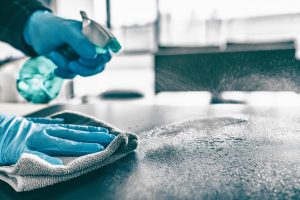 Cleaning home table sanitizing kitchen table surface with disinfectant spray bottle washing surfaces with towel and gloves. COVID-19 prevention sanitizing inside.