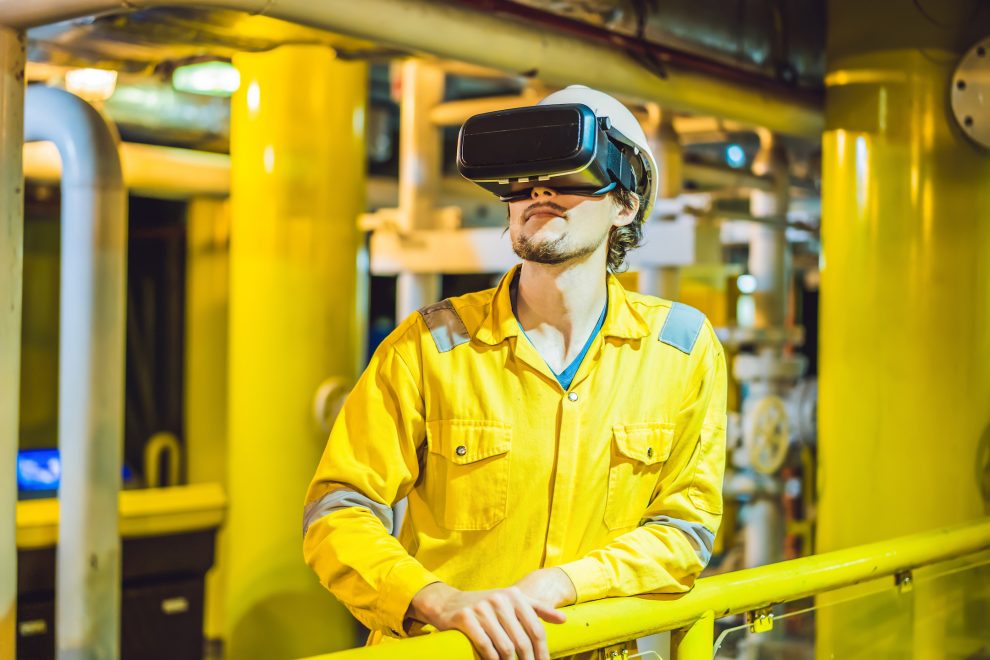 Young woman in a yellow work uniform, glasses and helmet uses virtual reality glasses in industrial environment,oil Platform or liquefied gas plant.