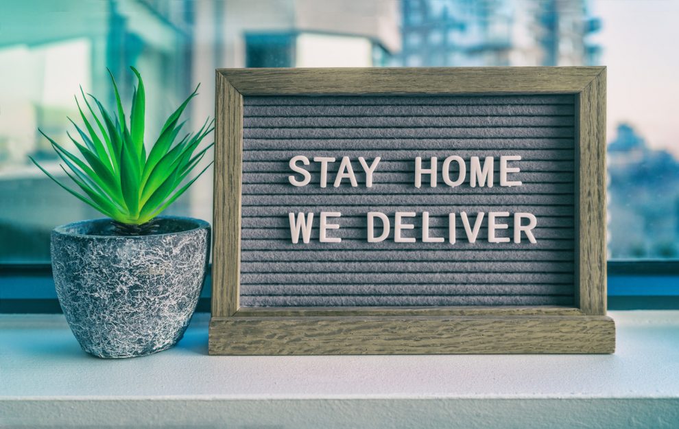 "STAY HOME WE DELIVER" Coronavirus social distancing restaurant business message sign. COVID-19 online delivery to home, staying inside. Grey felt board with plant.