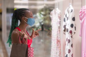 young African American woman at shopping mall in new normal after covid-19 - happy and beautiful black girl in face mask holding shopping bags enjoying at beauty fashion store